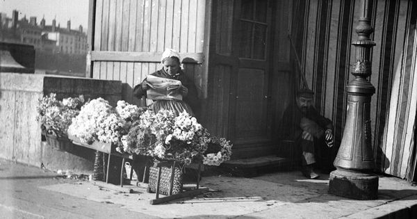 Marchande à fleurs à l'entrée d'un pont : photo négative NB sur plaque de verre au gélatino-bromure d'argent (vers 1900, cote : 10PH/61)